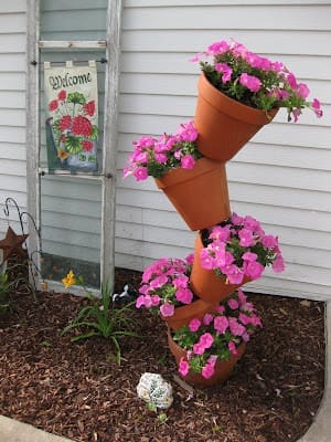 Terracotta pots stacked at an angle with pink geraniums inside